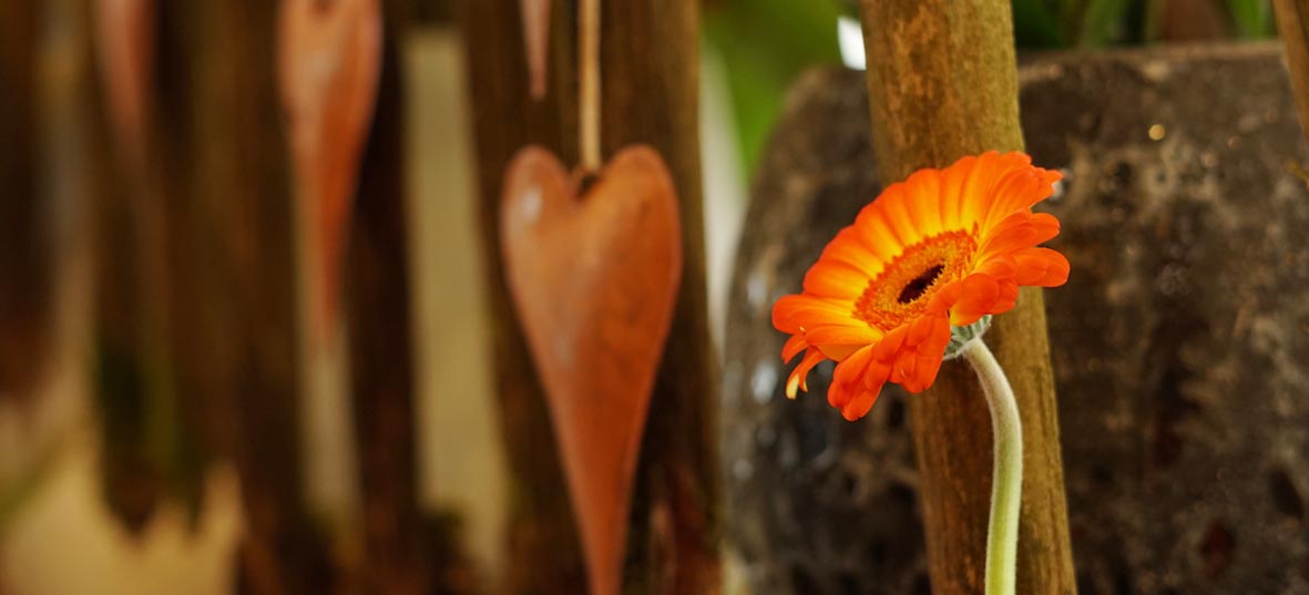 Blumen Art Manufaktur: rot/orange Gerbara, rostiges Deko-Herz im Hintergrund