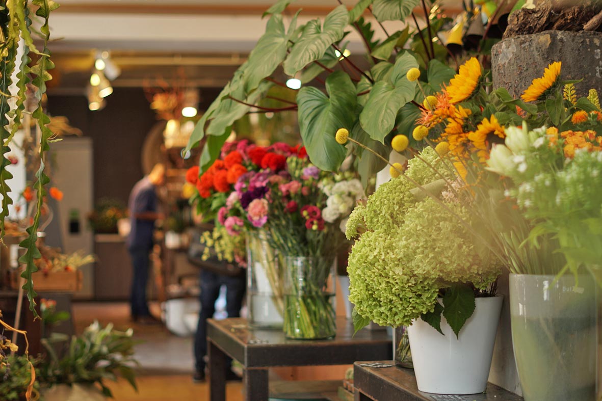 Blumen Art Manufaktur: Blick in Laden mit Blumen und im Hintergrund Personen